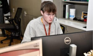 A student worker of JC in the IT solution center department working on a computer while wearing a headset.