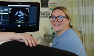 A Jackson College Sonographer Student smiling at the camera as she has the doopler on a patient and the screen in front of her.