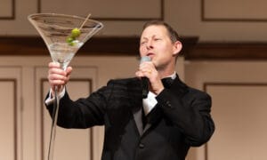 Matt Walch singing into a microphone holding a giant martini glass.
