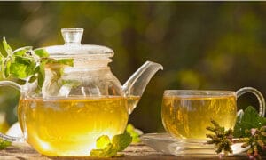A tea pot sitting on a table full of tea with a full tea cup next to it.
