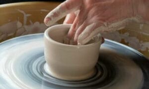 close up of clay pot on potters wheel with hand sculpting it