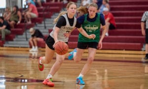 2 high school women's basketball players running with the basketball.
